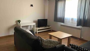 Una sala de estar con sofá, una mesa de centro, televisor sobre un mueble bajo y una ventana con cortinas.