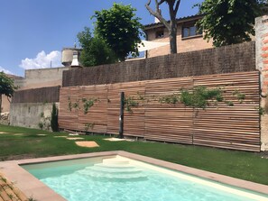 Una piscina con una valla de madera y un muro de ladrillo al fondo.
