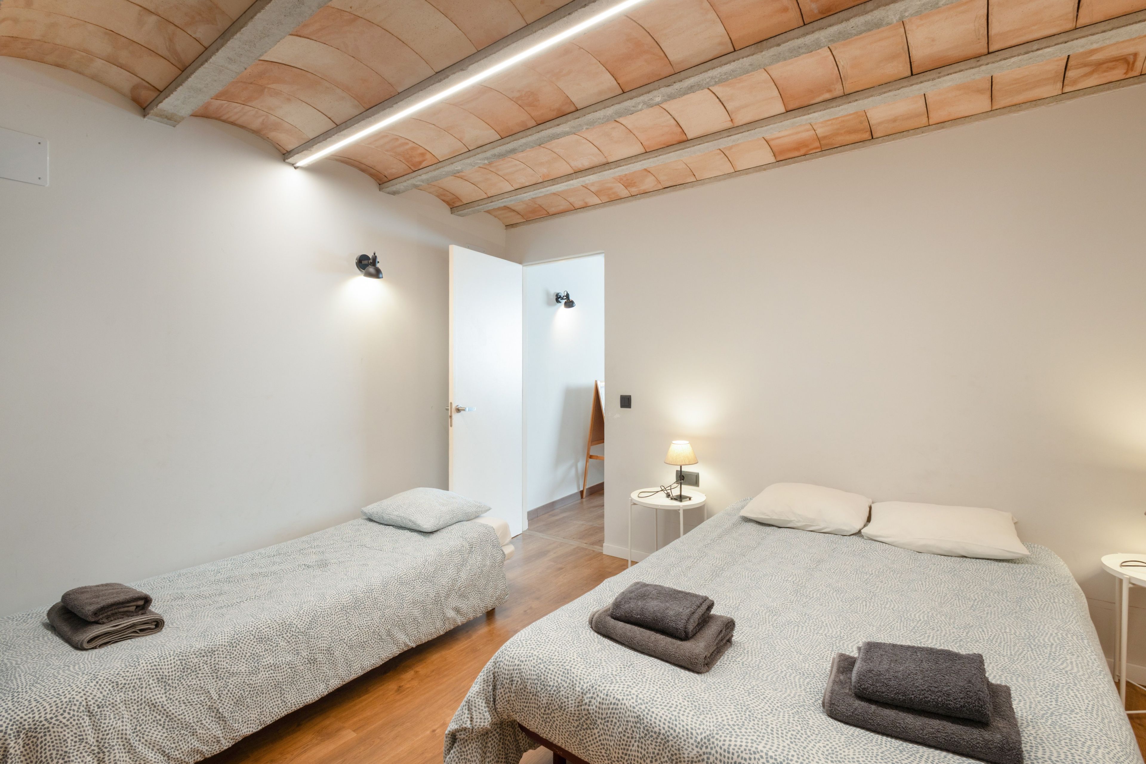 Une chambre d’hôtel avec deux lits simples, une petite table avec une lampe et un plafond en bois.
