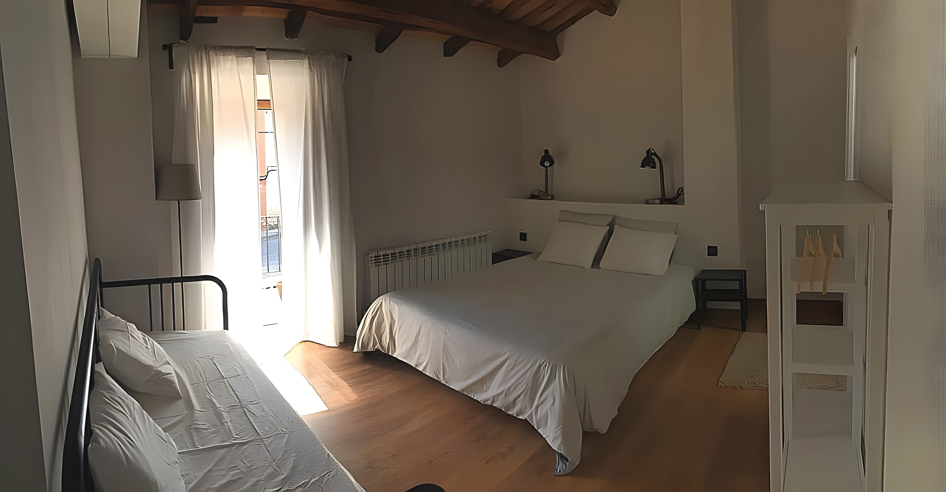 Un dormitorio con una cama, mesita de noche, lámpara y ventana con cortinas.