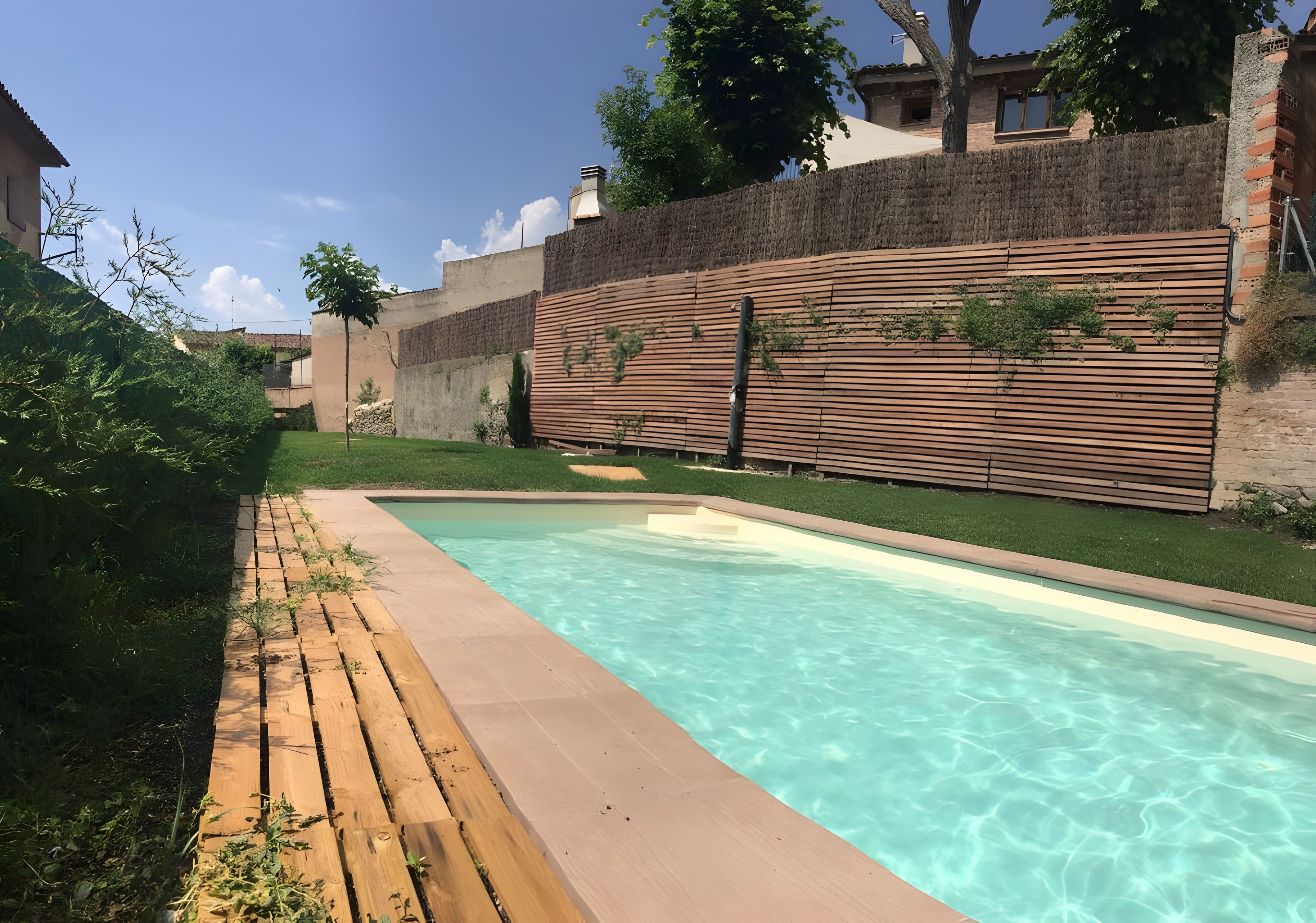 En swimmingpool med en træterrasse og en murstensvæg i baggrunden.
