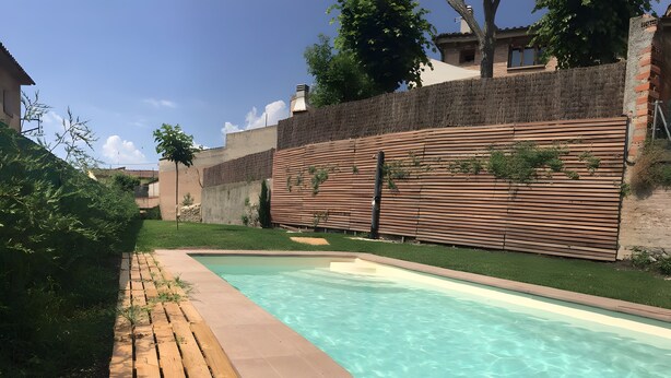 En swimmingpool med en træterrasse og en murstensvæg i baggrunden.