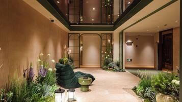 Un hall de hotel con un sofá verde, plantas decorativas y una pequeña mesa con dos faroles.