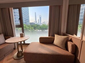 Une chambre d’hôtel moderne dotée d’une grande fenêtre, d’un canapé, d’une petite table et offrant une vue sur le paysage urbain.