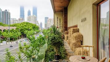 A balcony with a view of a cityscape, a table with a cup, and a potted plant.