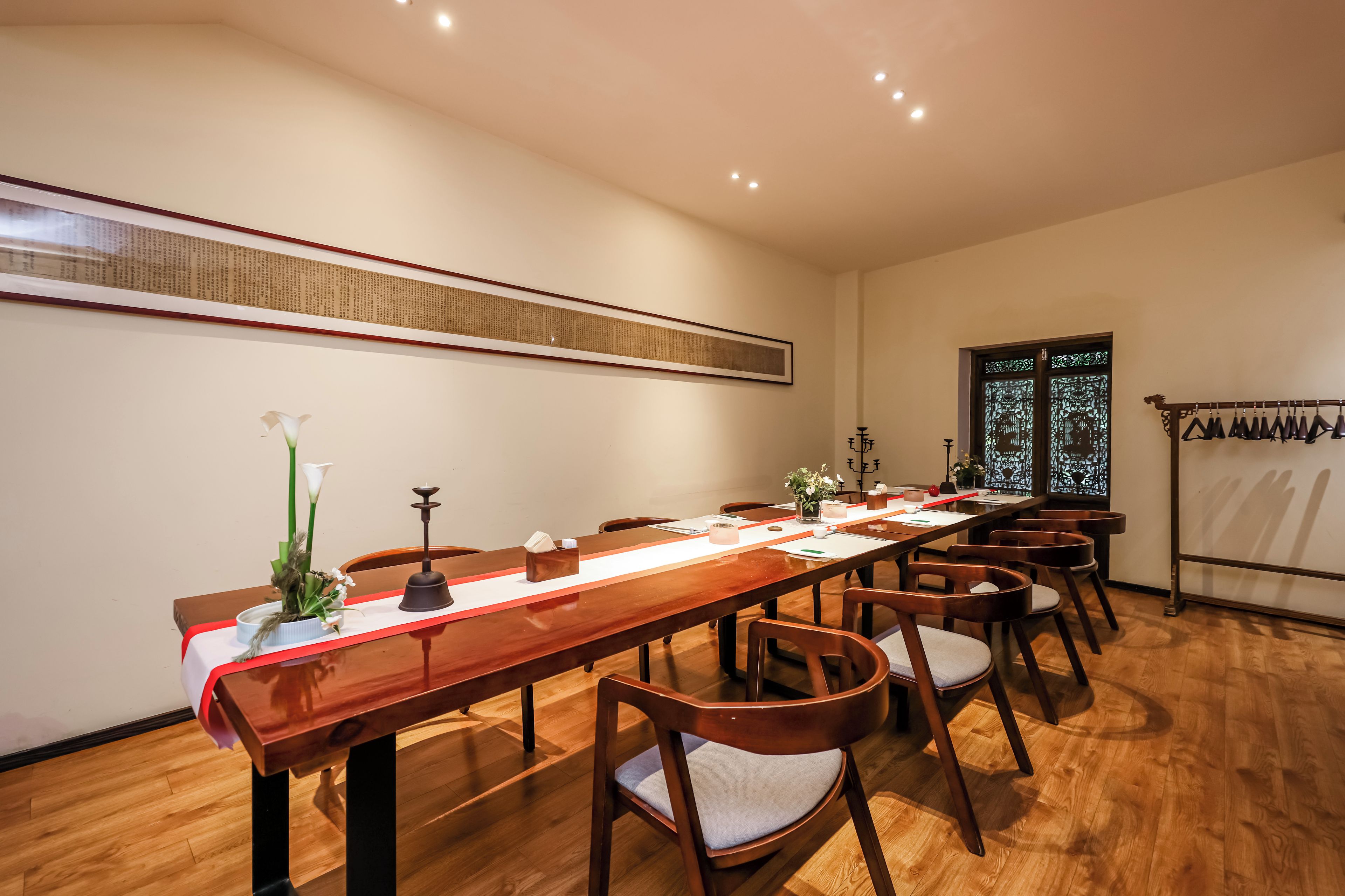 Un salón de conferencias con una larga mesa de madera, sillas, un jarrón decorativo y un tapiz tradicional chino.