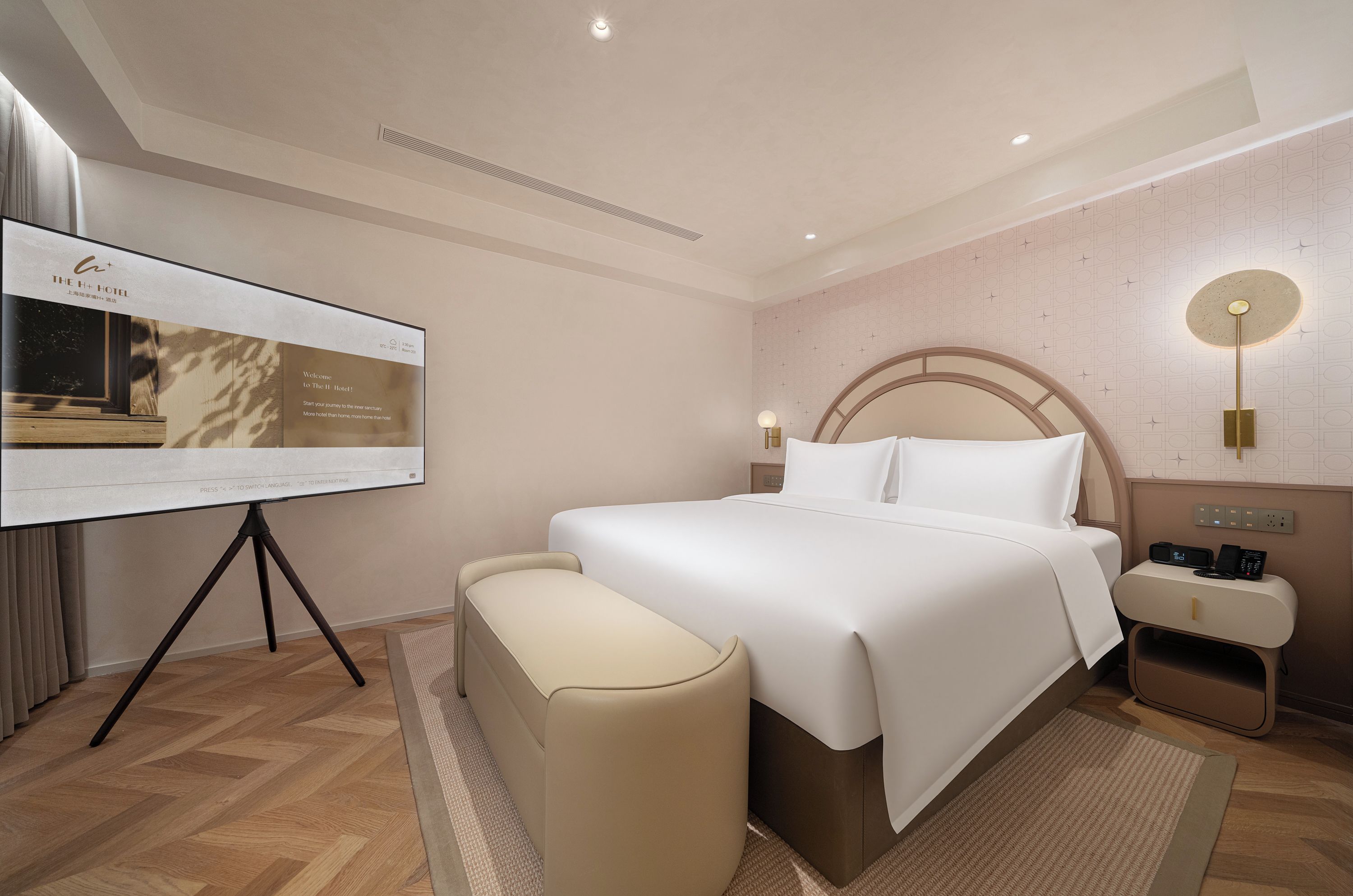 Habitación de hotel con una cama grande, mesitas de noche, un escritorio con una computadora y una pantalla de proyección mostrando información del hotel.