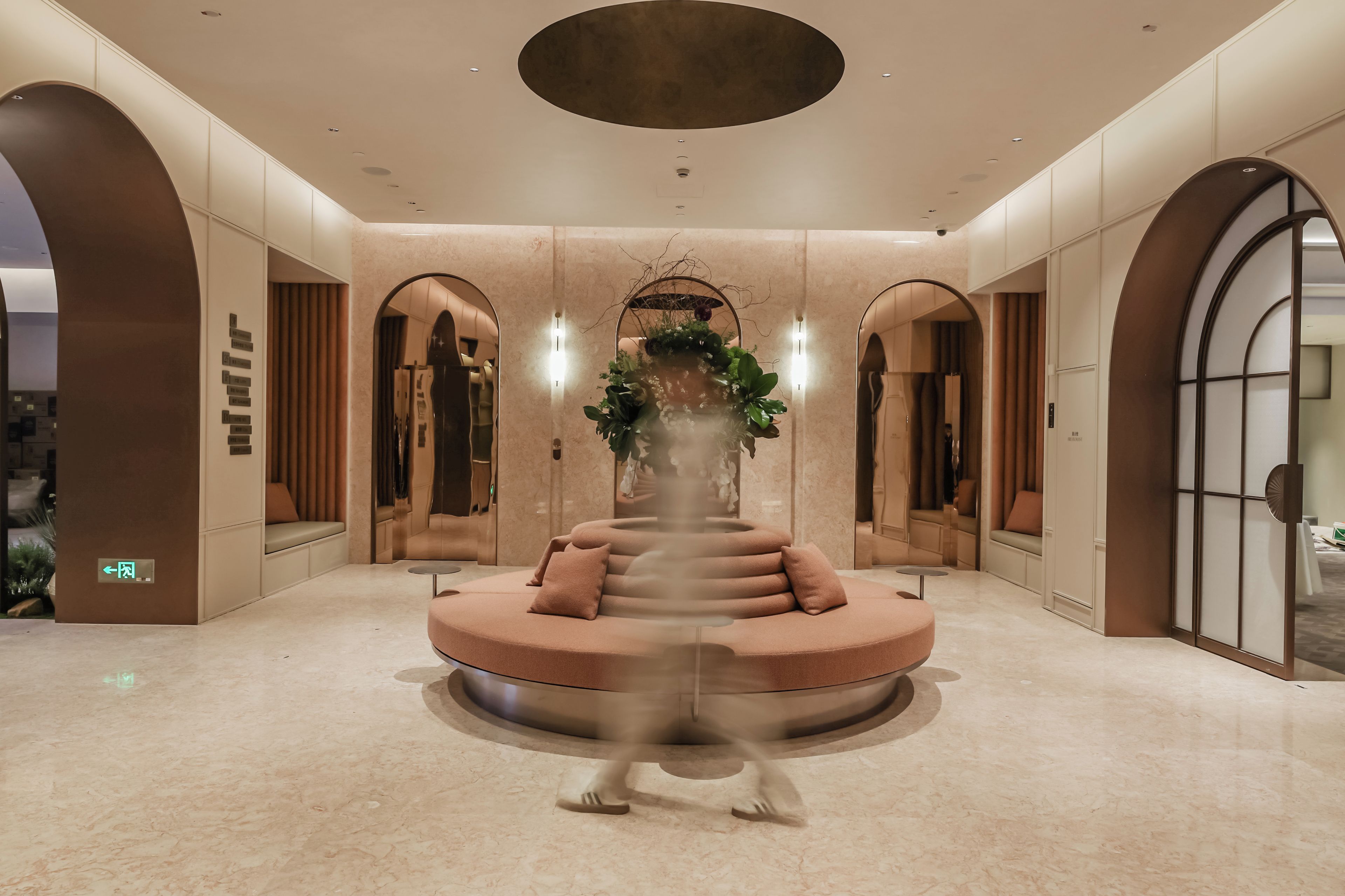 A modern lobby with a central seating area, mirrored walls, and a ceiling with recessed lighting.
