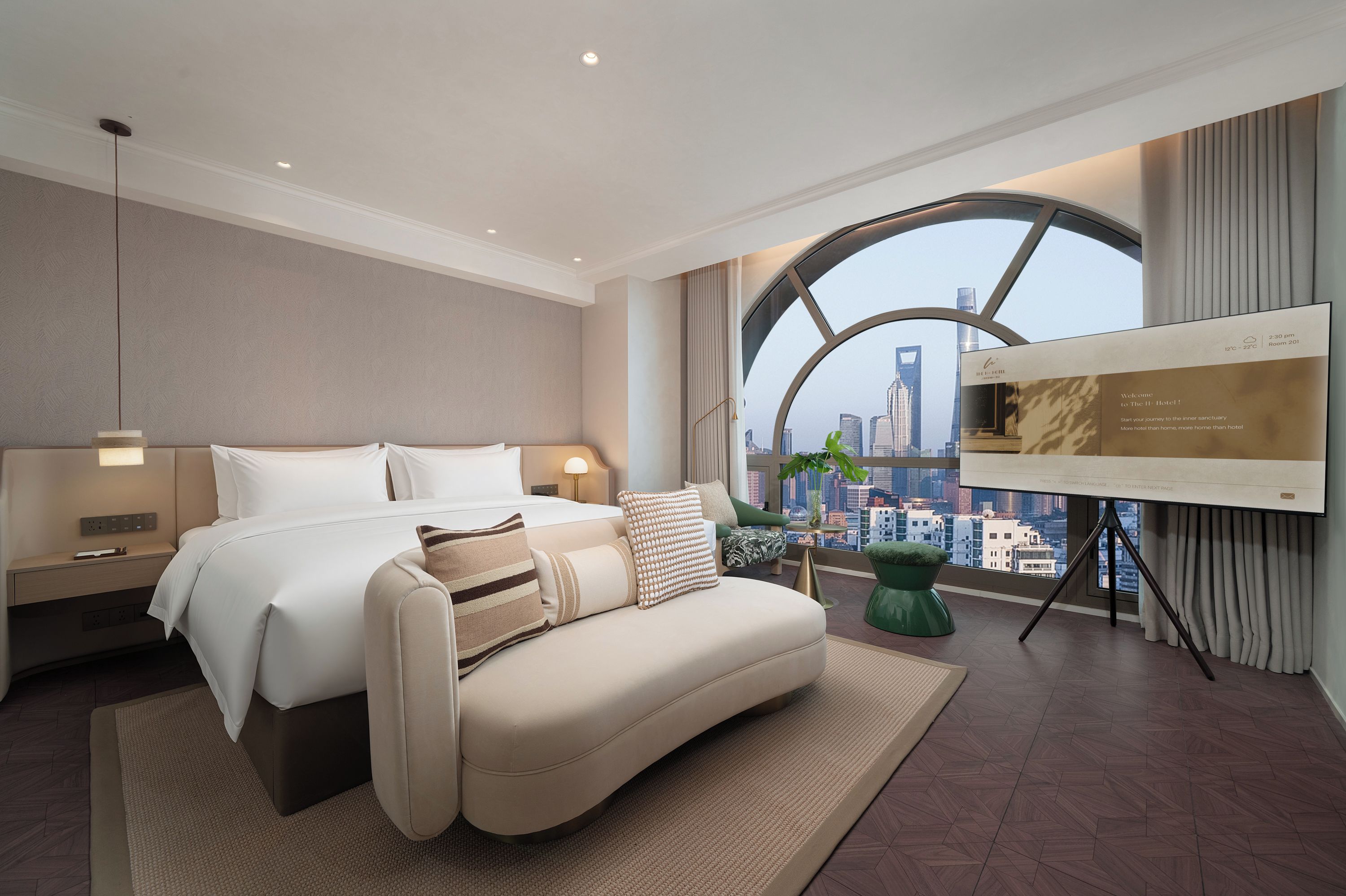 Habitación de hotel moderna con cama, sofá, televisión y un ventanal con vistas a la ciudad.