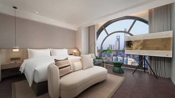 Habitación de hotel moderna con cama, sofá, televisión y un ventanal con vistas a la ciudad.