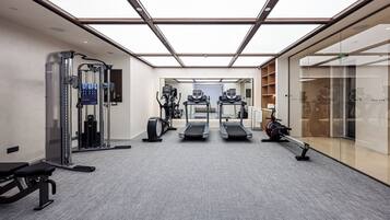 Un gimnasio moderno con equipo de ejercicio, un muro espejado y una puerta de cristal que da a un pasillo.