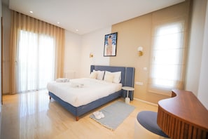 A modern bedroom with a large bed, bedside tables, a small round table, and a view of the outdoors through the window. - Villa Apollon: Seaside and Luxurious (La Marsa)