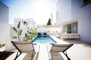 A pool area with lounge chairs, a wooden fence, and white buildings. - Villa Apollon: Seaside and Luxurious (La Marsa)