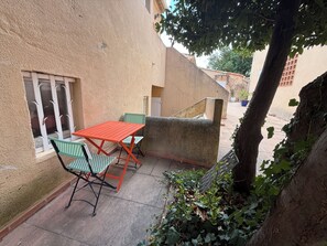 Un patio con una mesa y sillas, una ventana con rejas y un árbol con enredaderas.
