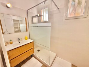 Un baño moderno con ducha envuelta en vidrio, tocador de madera y un espejo grande.