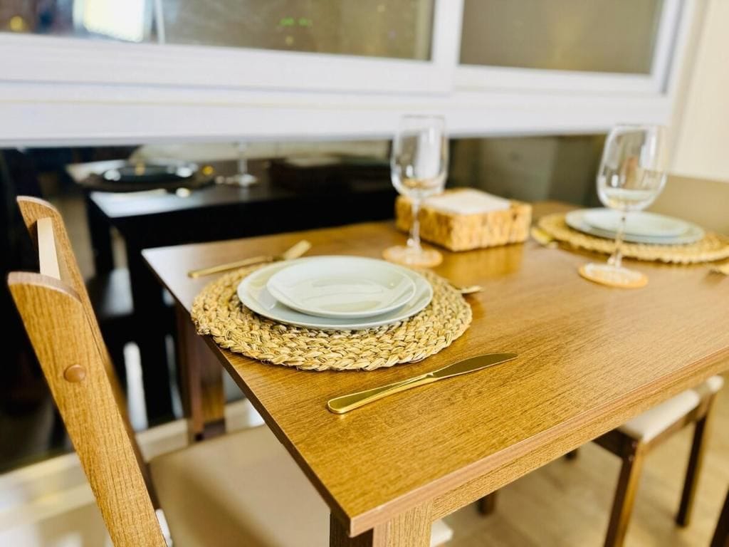 Een houten eettafel met een geweven placemat, een bord, een mes en twee glazen witte wijn.