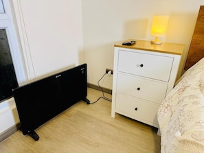 Un dormitorio con cama, mesita de noche con lámpara, cómoda blanca y radiador.