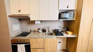 Een praktische keuken met een kookplaat, magnetron en spoelbak. Boven het aanrecht zijn kastjes en eronder een kleine oven.