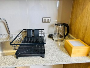 Una cocina con un lavamanos de acero inoxidable, una cafetera y un escurreplatos negro.