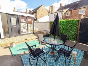 A patio with a round table and four chairs, a black umbrella, and a green leafy wall. - The Old Bank House (Morpeth)