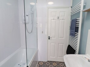 A bathroom with a glass-enclosed shower, a white door, and a white sink with a towel rack. - The Old Bank House (Morpeth)