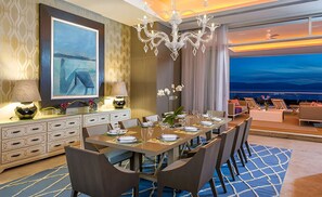 A hotel dining area with a long table set for a meal, a chandelier, and a view of the cityscape. -  4BR Residence The Grand Luxxe In Vidanta Nuevo Vallarta (Nuevo Nayarit)