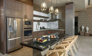 A modern kitchen with stainless steel appliances, a marble island, and wooden chairs. -  4BR Residence The Grand Luxxe In Vidanta Nuevo Vallarta (Nuevo Nayarit)