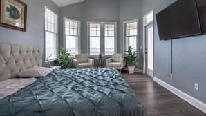 Ein Schlafzimmer mit einem großen Bett, zwei Stühlen, einem Fernseher und einem Fenster mit Jalousien.
