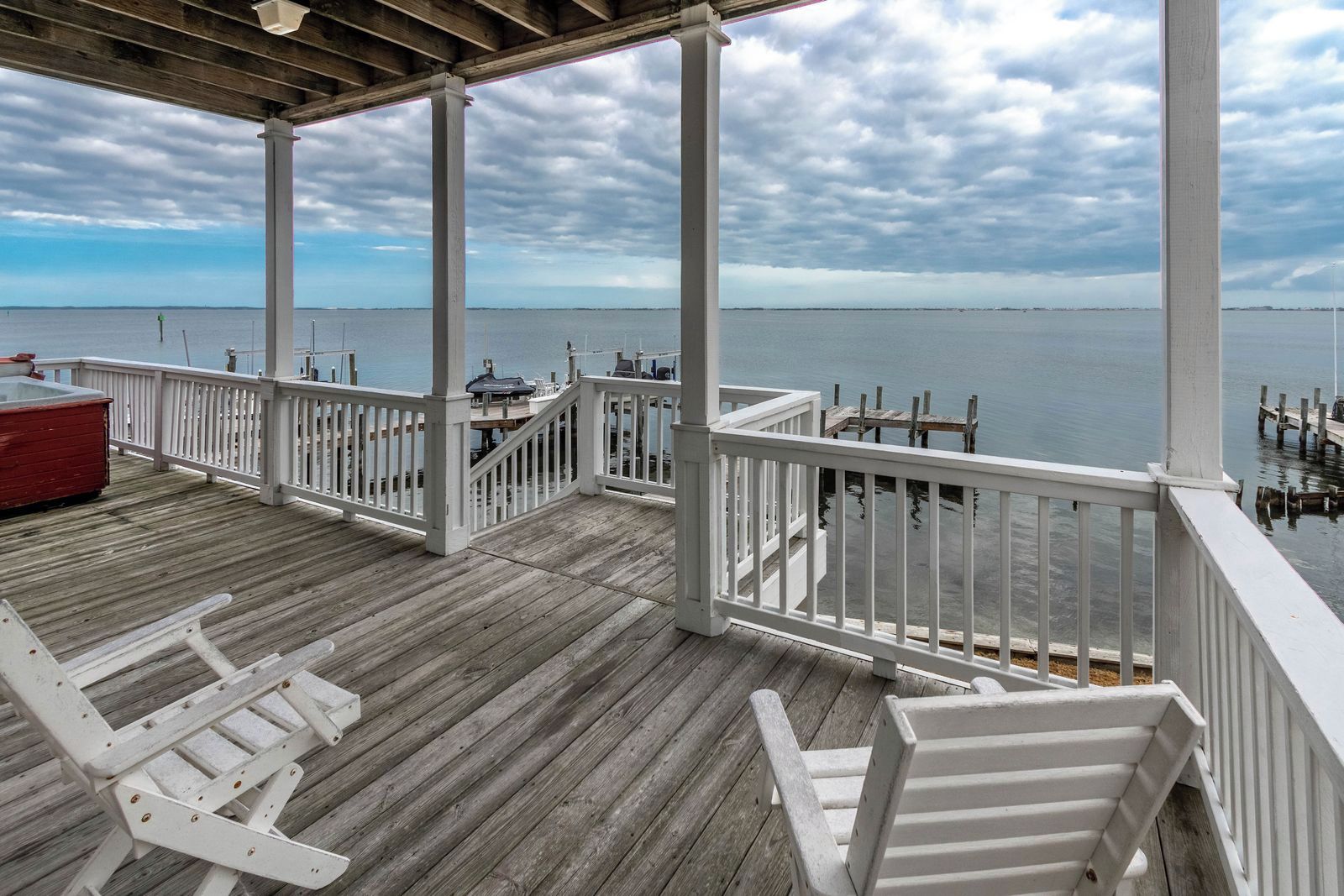 A wooden deck with white railings overlooking a calm body of water.