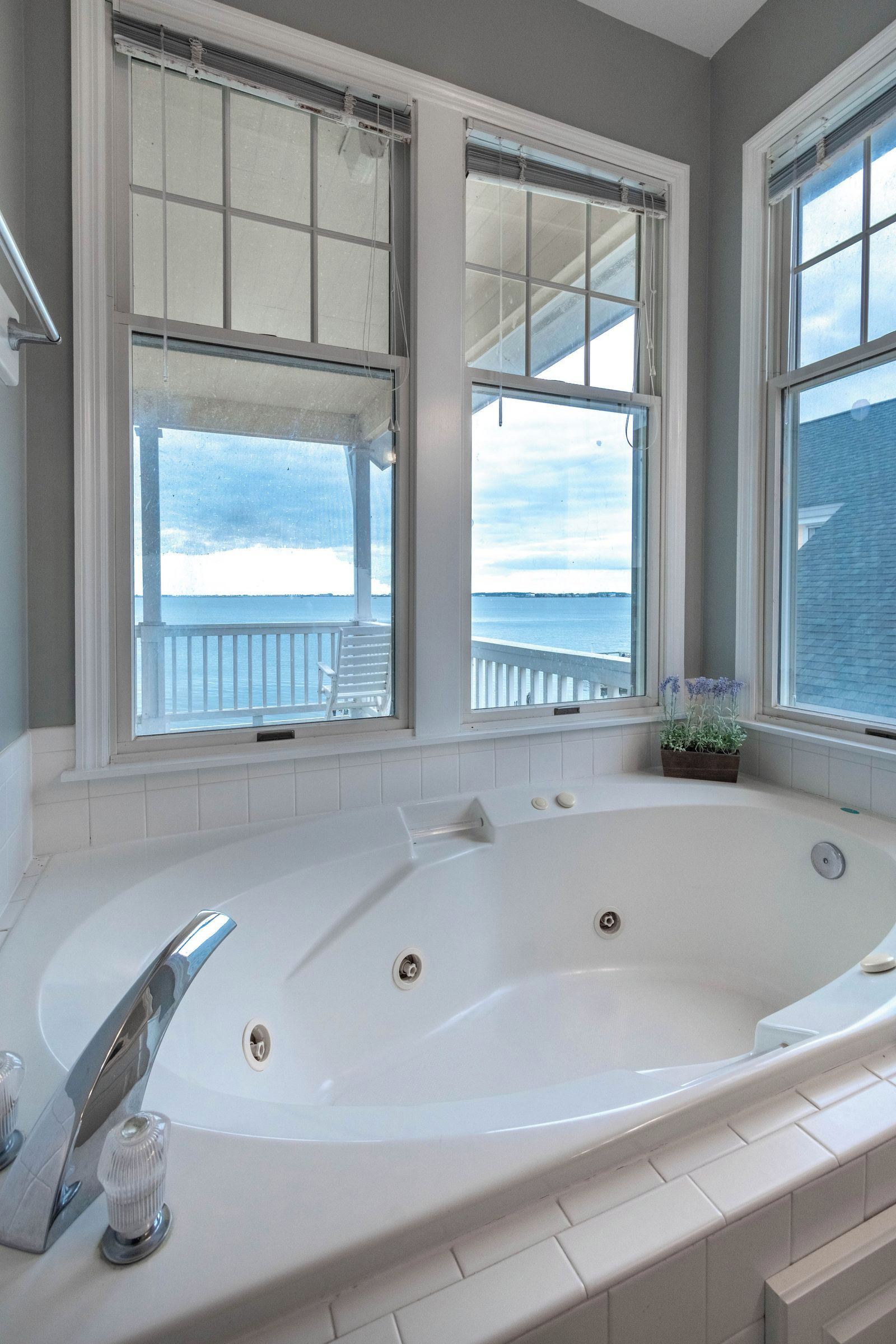 A bathroom with a large bathtub, a window with a view of the sea, and a small plant on the windowsill.
