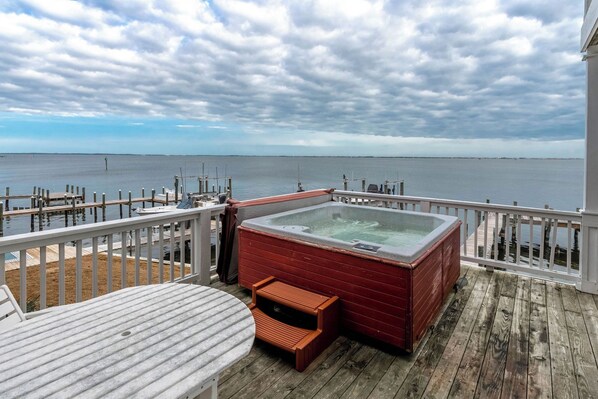 A wooden deck with a hot tub, a table, and a view of the water.