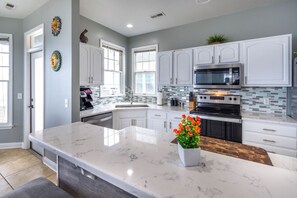 A modern kitchen with white cabinets, a large island, a microwave, and an oven.