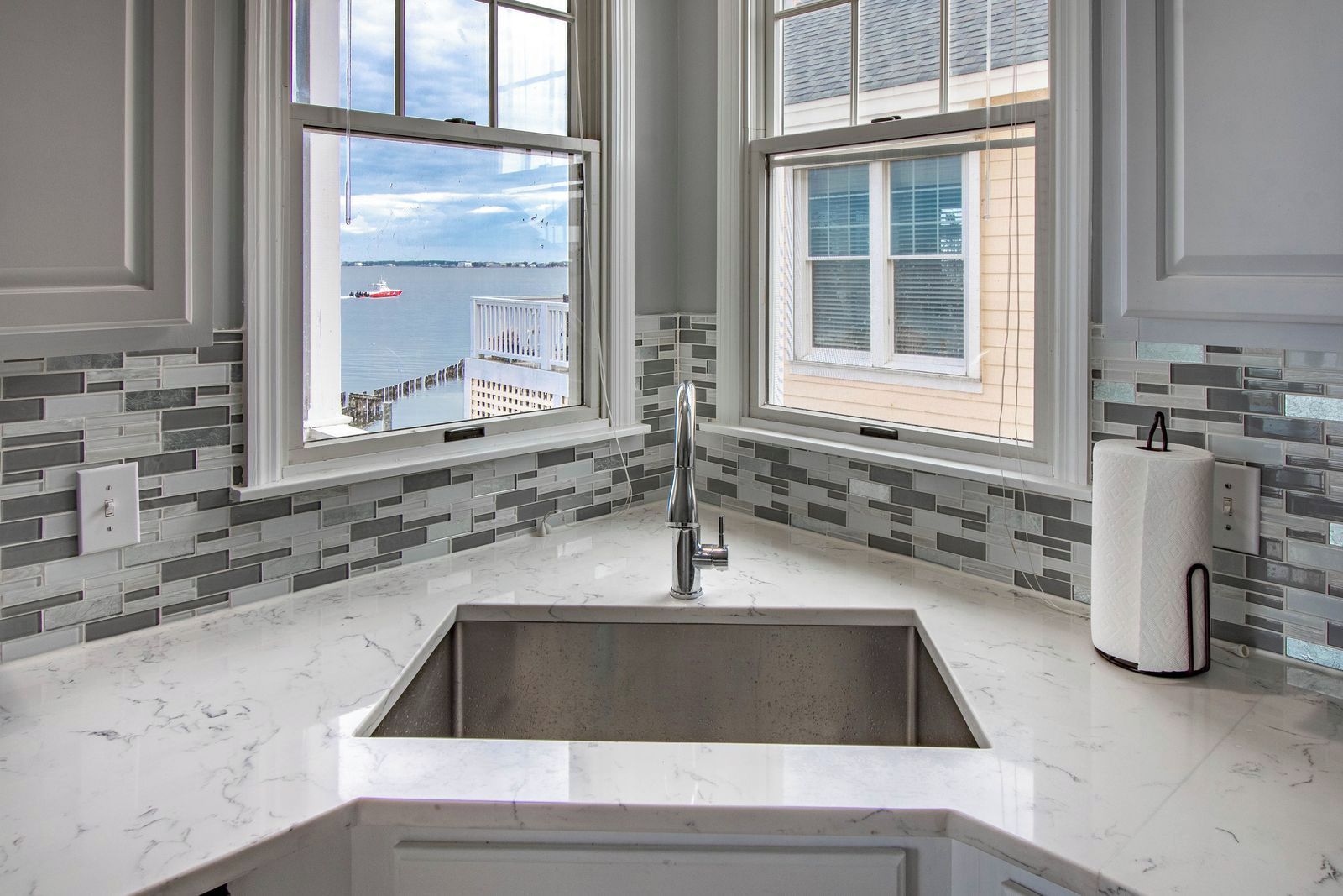 Et køkken med en stor vask, to vinduer med havudsigt og et flisebeklædt backsplash.