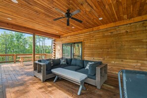 A covered deck with a wooden ceiling and a ceiling fan, a gray sectional sofa with cushions, and a wooden table. - New Pet Friendly Home w HotTub, FirePit, PoolTable (McHenry)