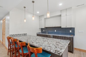 A modern kitchen with a granite countertop, wooden chairs, and pendant lighting. - New Pet Friendly Home w HotTub, FirePit, PoolTable (McHenry)