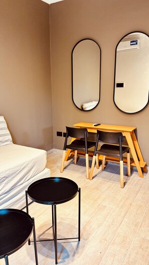 A room with a bed, a desk with two chairs, a round table, and two wall mirrors.