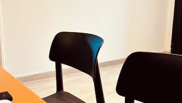 Una habitación con una televisión de pantalla plana montada en la pared, dos sillas negras y una mesa naranja.