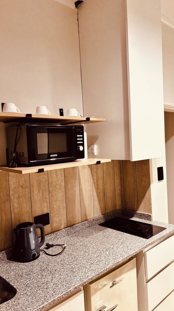 A kitchen with a microwave on a wooden shelf, a kettle on the countertop, and a stove.