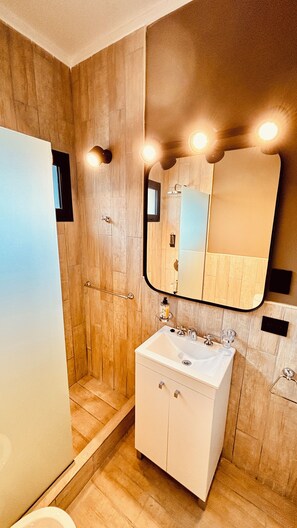 A modern bathroom with a wooden wall, a white sink, and a mirror with lights above it.