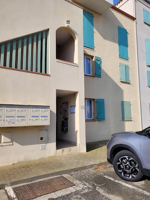 A building with multiple balconies, mailboxes, and a parked car.