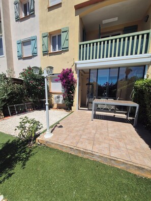 Un edifici residencial amb un balcó, un pati amb taula i cadires, i una zona de jardí amb gespa i arbustos.