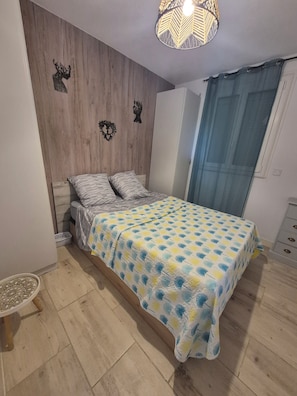 A bedroom with a bed, wooden wall paneling, a decorative ceiling light, and a window with curtains.