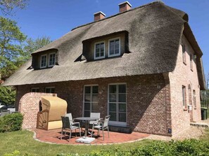 A brick house with a thatched roof, a patio with chairs, and a small garden. - Semi-detached House "oasis 3" (St. Peter-Ording)