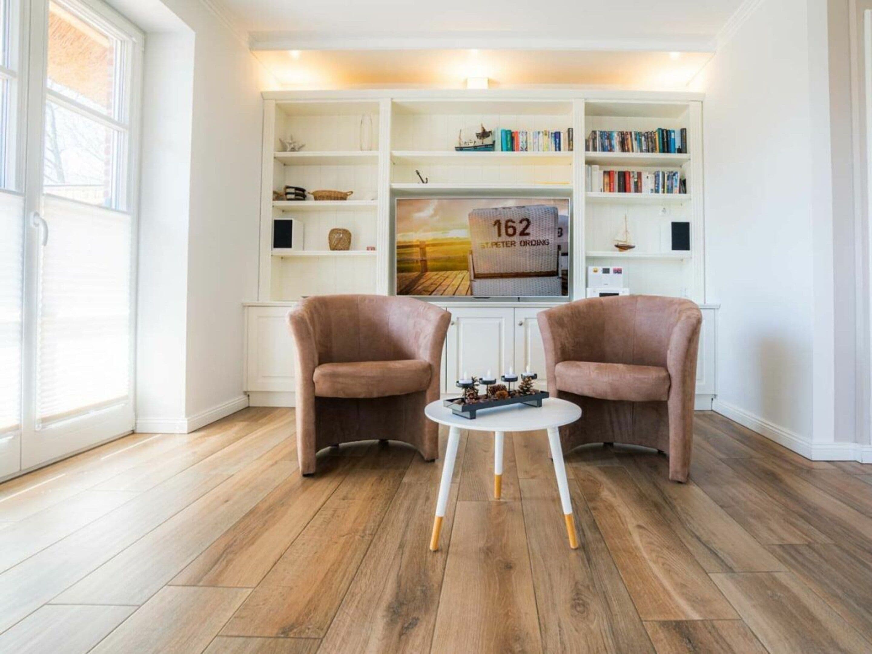 Un salon avec deux fauteuils, une petite table et une bibliothèque contenant des livres et des objets décoratifs.