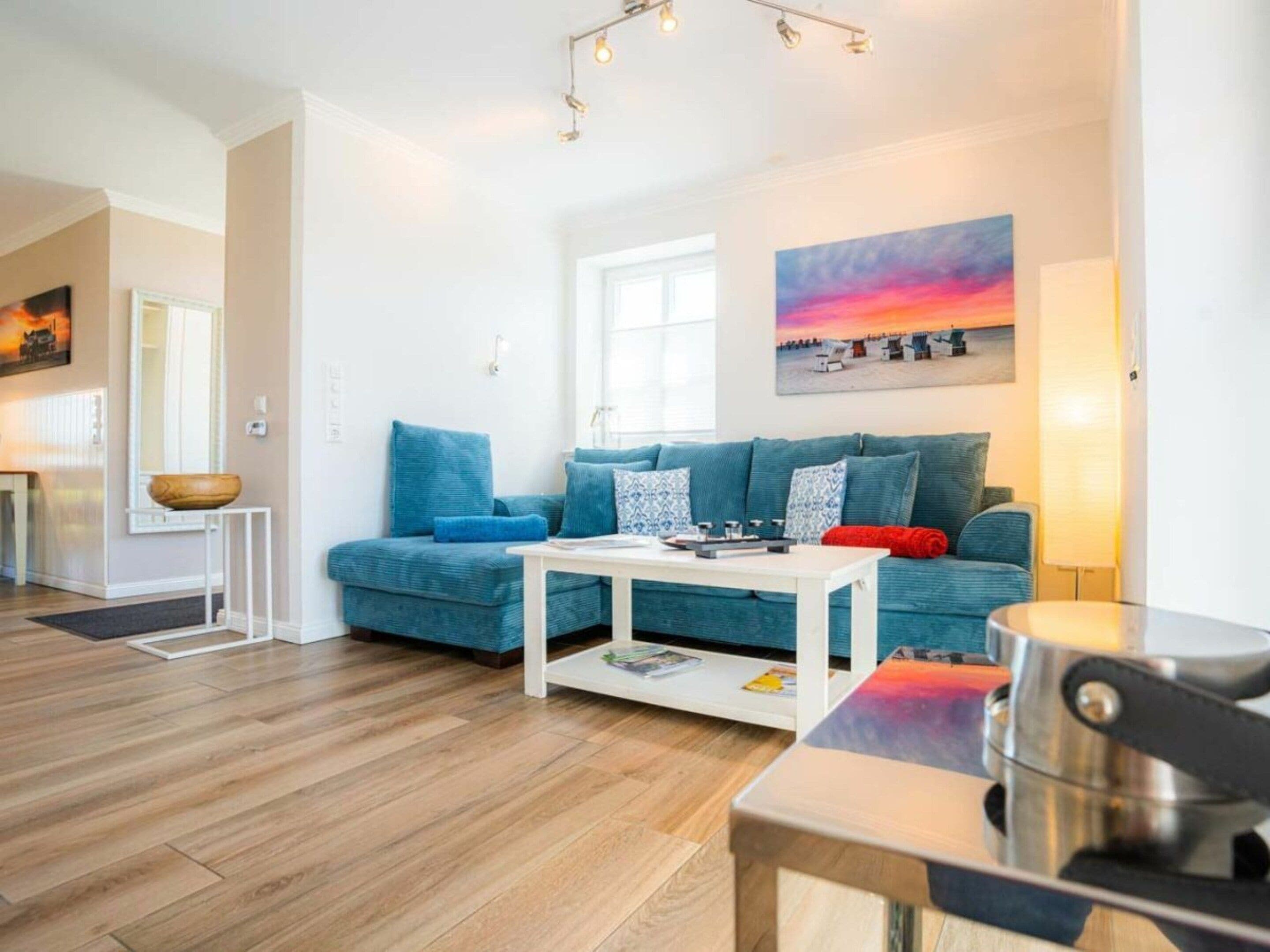 A modern living room with a blue sofa, a white coffee table, and a painting of a sunset.