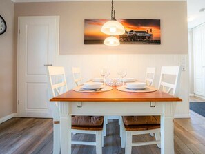 A dining area with a wooden table set for four, white chairs, and a pendant light. - Semi-detached House "oasis 3" (St. Peter-Ording)