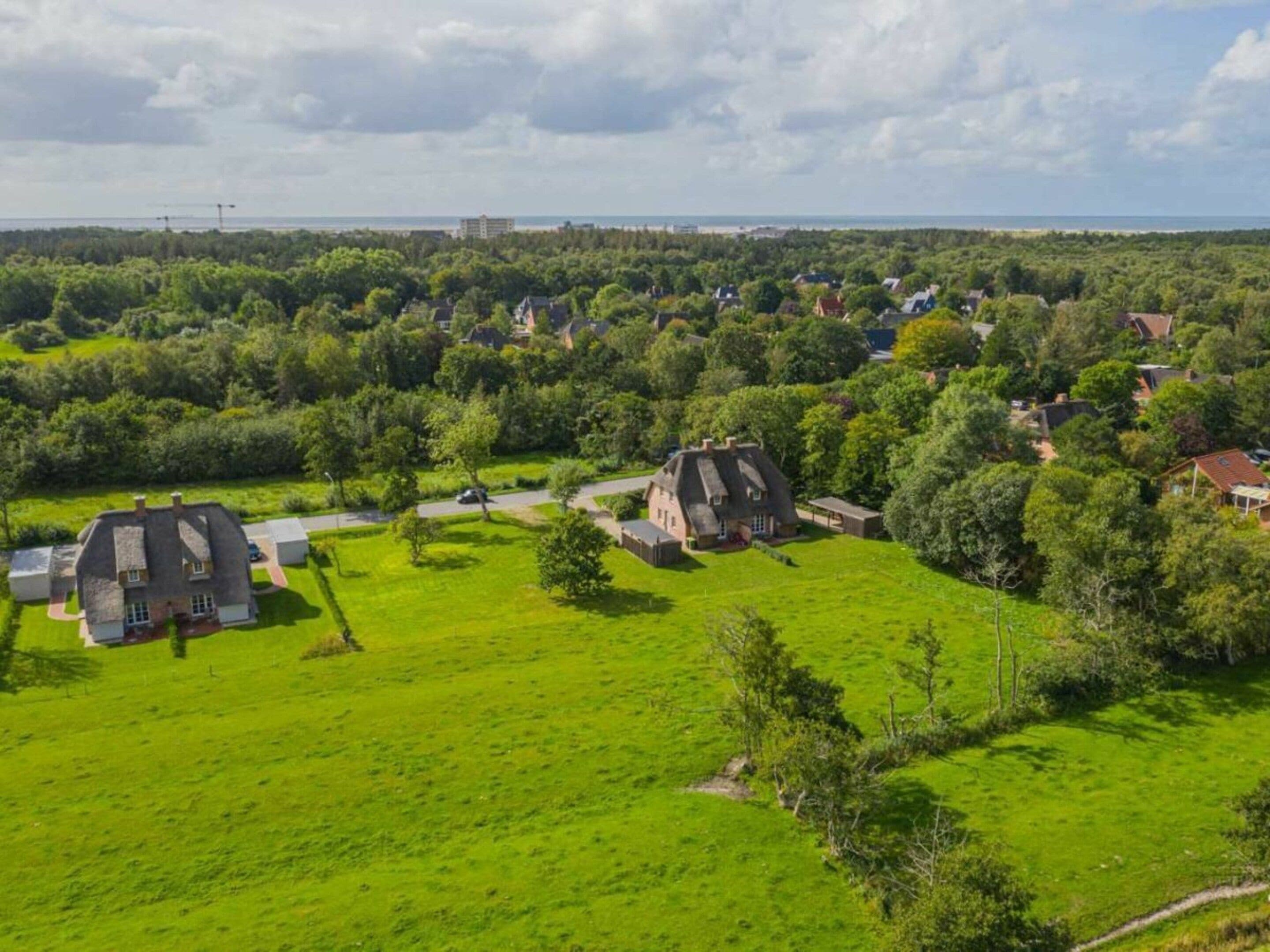 Un quartier résidentiel avec des maisons, un grand espace vert et une vue lointaine sur la mer.