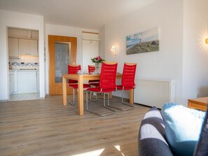 A dining area with a wooden table and red chairs, a kitchen with white cabinets, and a painting on the wall. - Apartment 14 (St. Peter-Ording)