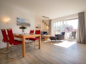 A modern living space with a dining area, seating arrangement, and large windows offering a view. - Apartment 14 (St. Peter-Ording)