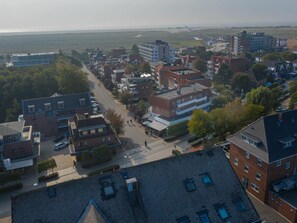 An aerial view of a residential area with multiple buildings, streets, and a distant view of a coastline. - Apartment 14 (St. Peter-Ording)